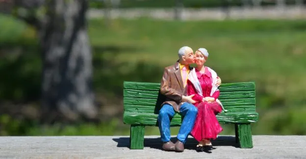 Statue of a couple sitting on a bench while the man kisses the women on the cheek